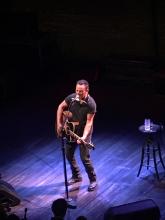 Bruce Springsteen playing guitar on stage.  A stool with a glass of water in the background.